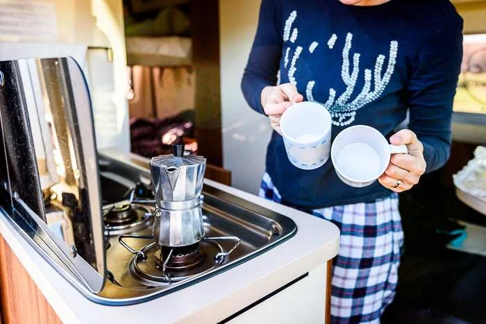stove in a self contained campervan as a woman makes coffee